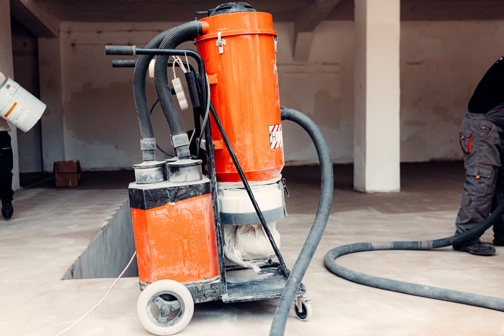 Construction workers applying epoxy coating on concrete floor and using industrial vacuum cleaner