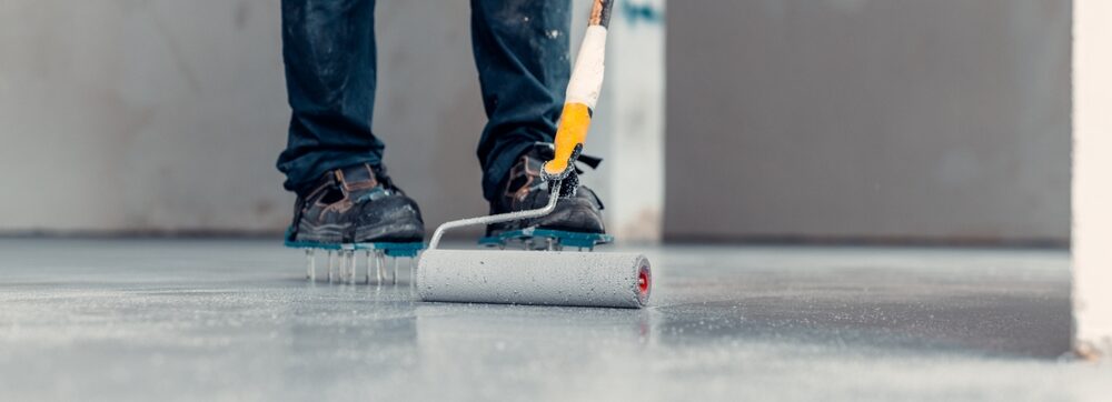 A construction worker apply grey epoxy resin in an industrial hall